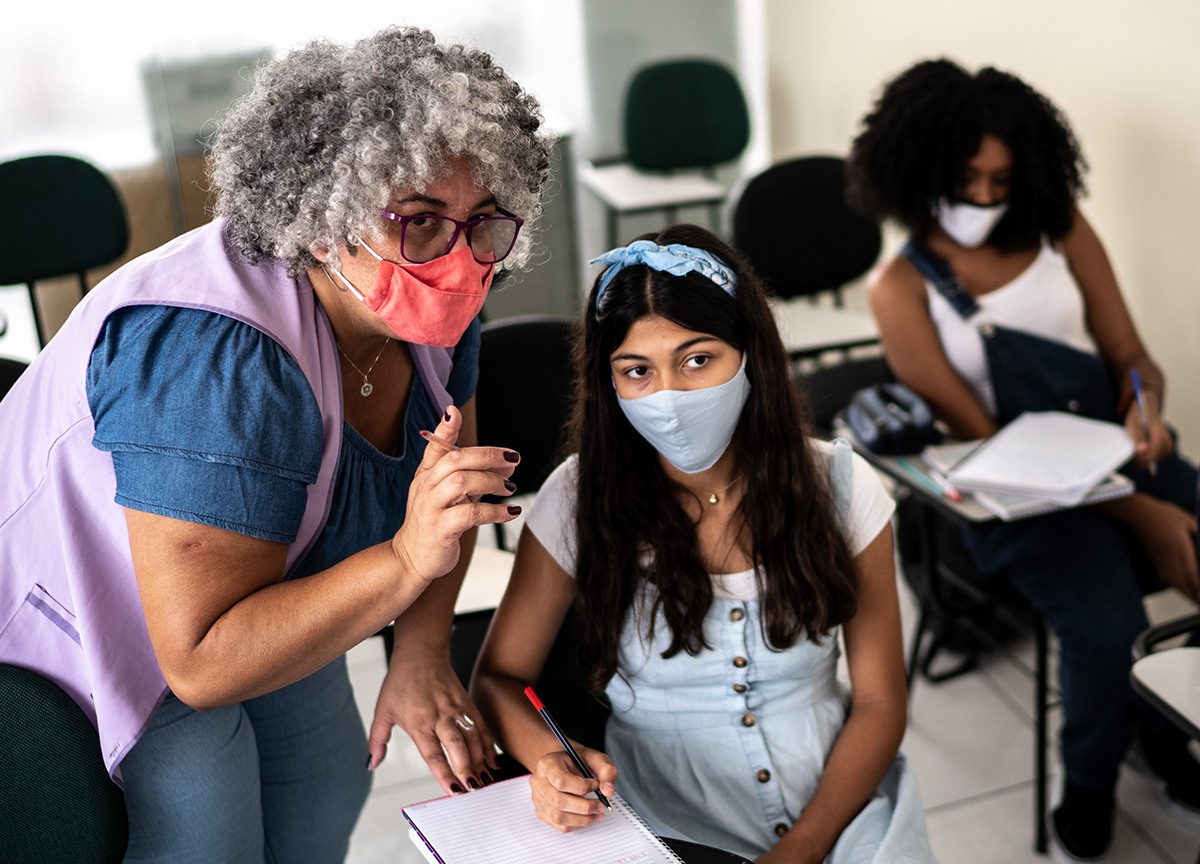 Teacher is assisting a student, both are wearing masks